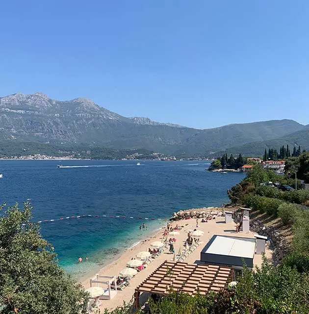 Strand an der Bucht von Luštica mit klarem Wasser, Bergen im Hintergrund und Badegästen
