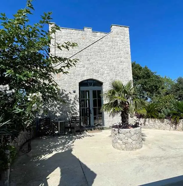 Steinerner Turm mit Eingangstür, umgeben von mediterranen Pflanzen und Palmen