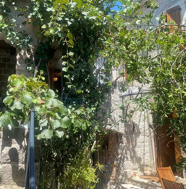 Bewachsenes Steinhaus mit Holztür, Balkon und mediterranen Pflanzen im Innenhof.