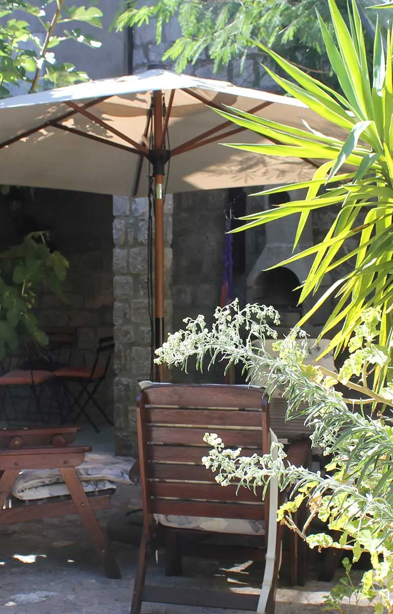 Gemütlicher Innenhof mit Sonnenschirm, Holzmöbeln und mediterraner Bepflanzung vor Steinhaus.