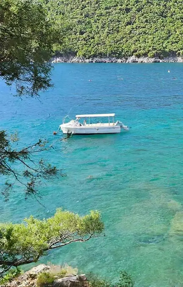 Türkisfarbene Bucht auf der Halbinsel Luštica mit Boot, Felsen und mediterraner Vegetation.