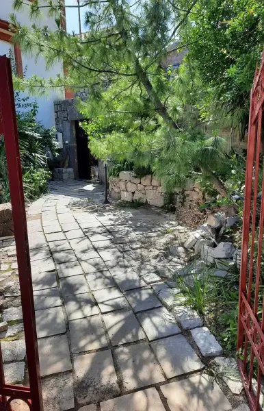 Gepflasterter Gartenweg mit Tor, B&auml;umen und Natursteinmauern im Sonnenschein