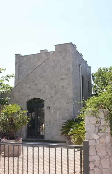 Exterior of a two-story stone house with gate, palms and sunlit garden