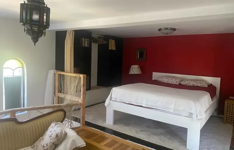 Open bedroom with red wall, double bed, seating area and gallery
