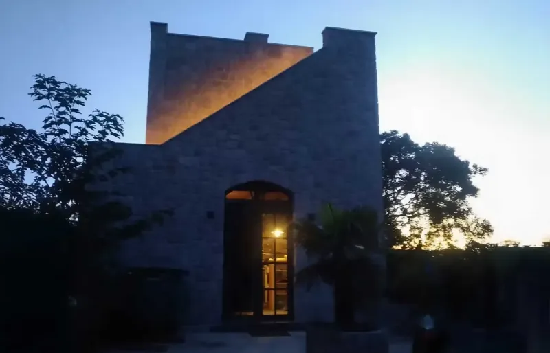 Stone house at dusk, warmly lit, with arched entrance and trees in the foreground