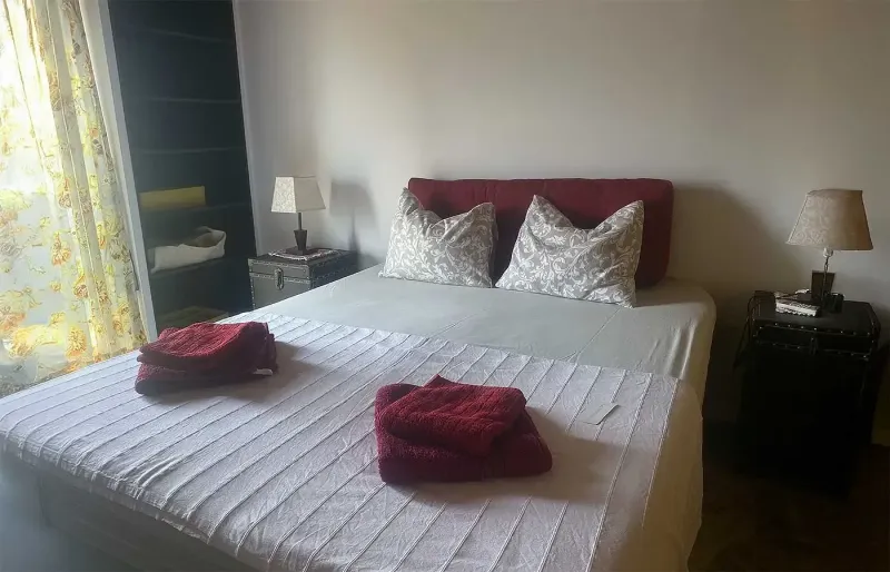 Bright bedroom with double bed, bedside tables and folded towels