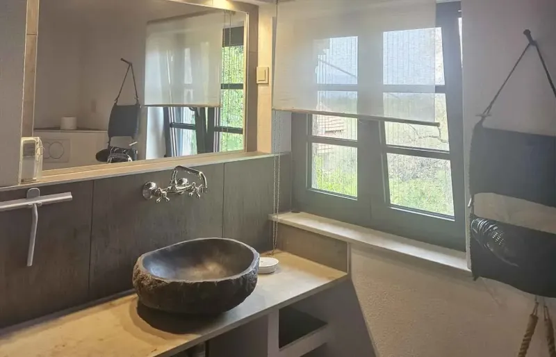 Modern bathroom with stone basin, mirror and green garden view