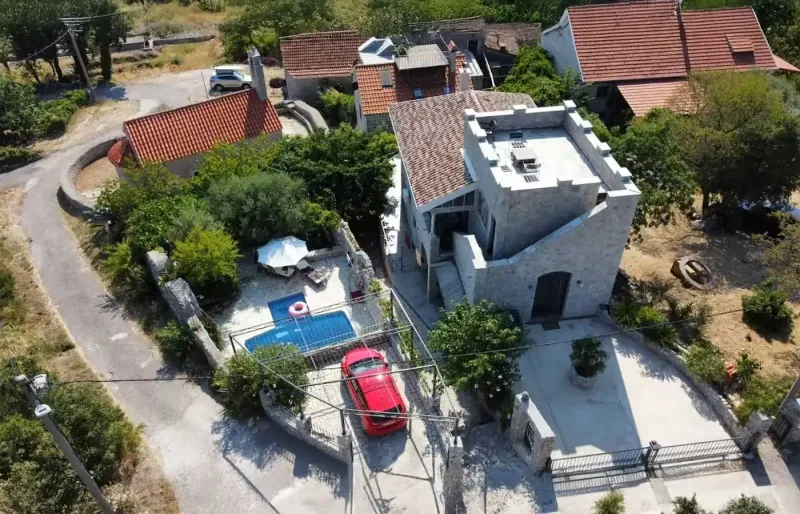 Aerial view of a stone house with courtyard, pool, terrace and parking in a green village setting