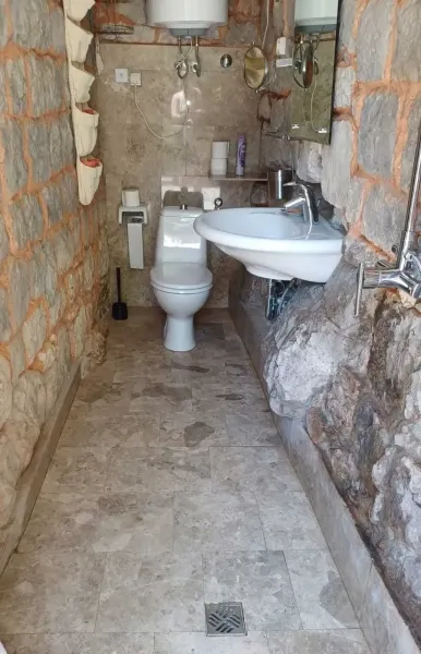 Small bathroom with toilet, sink, shower and natural stone walls