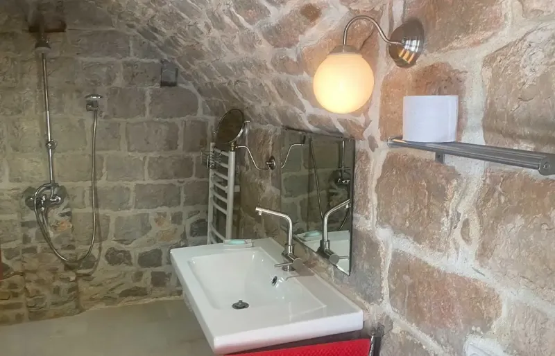 Badezimmer mit Natursteinw&auml;nden, Dusche, Waschbecken und sanfter Beleuchtung