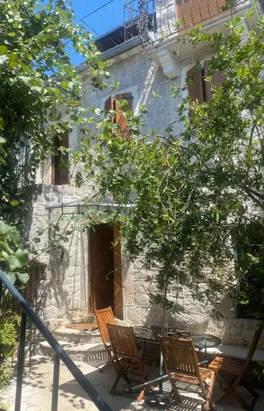 Schattiger Innenhof mit Holzm&ouml;beln, Steinfassade und mediterranem Gr&uuml;n