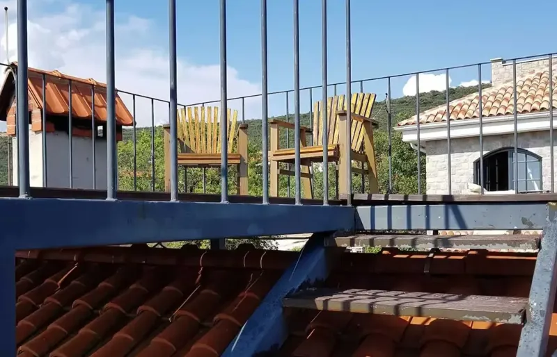 Dachterrasse mit Holzst&uuml;hlen, Metallgel&auml;nder und Blick &uuml;ber D&auml;cher und gr&uuml;ne H&uuml;gel
