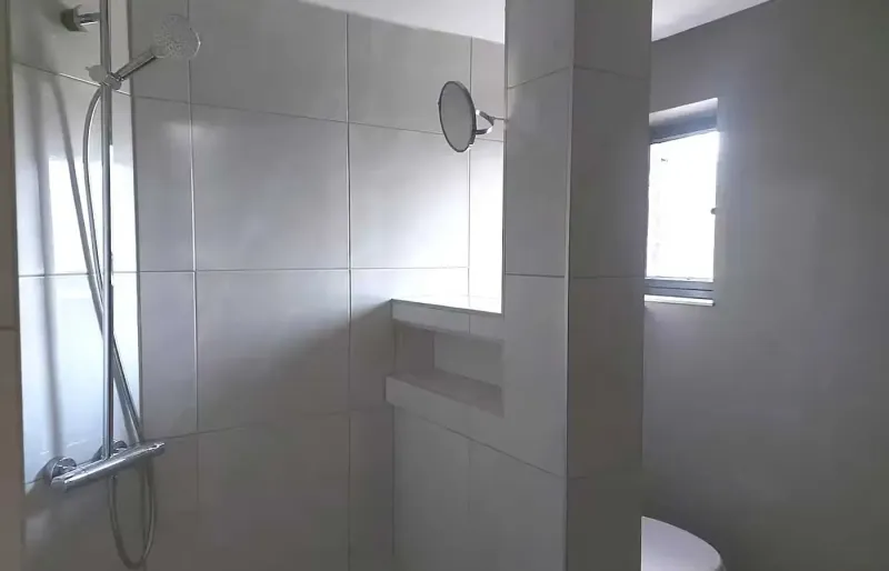 Helles Bad mit gefliester Dusche, Nische und kleinem Fenster