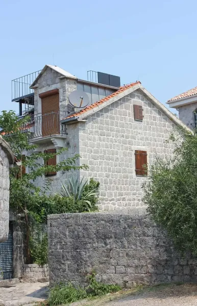 Exterior of a traditional stone house with wooden shutters, balcony and garden wall
