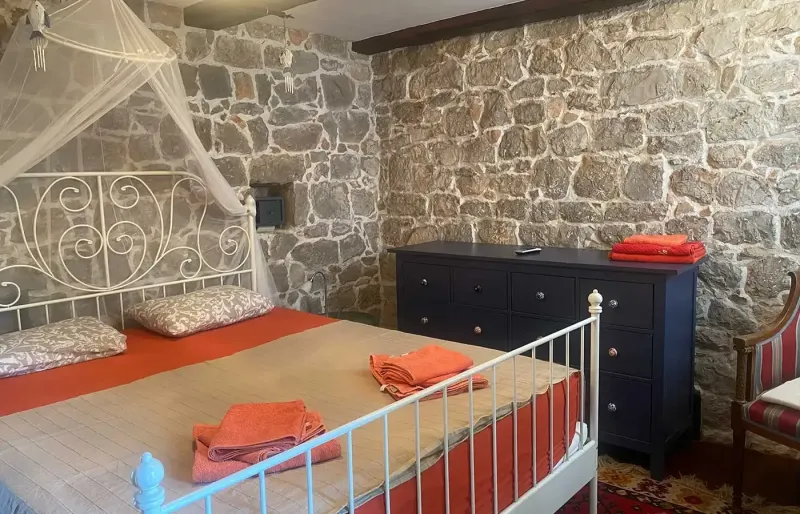Bedroom with metal bed, mosquito net, stone walls and folded towels